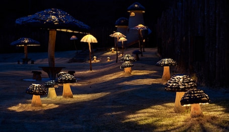 A pathway lined with mushroom-shaped structures, some with umbrellas, leading to a building with a dome-like roof.