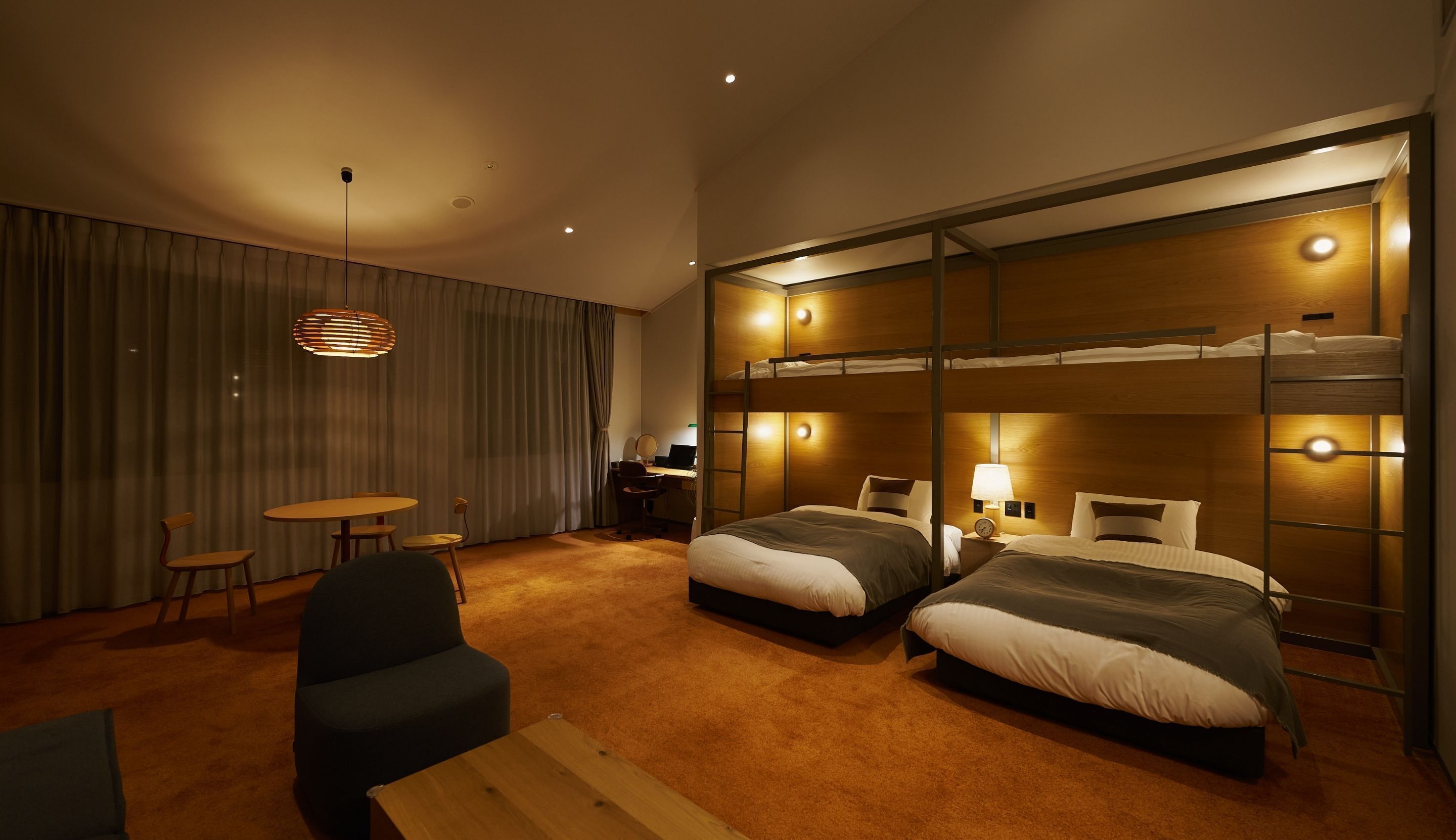 A hotel room with bunk beds, a desk, a chair, and a small table.