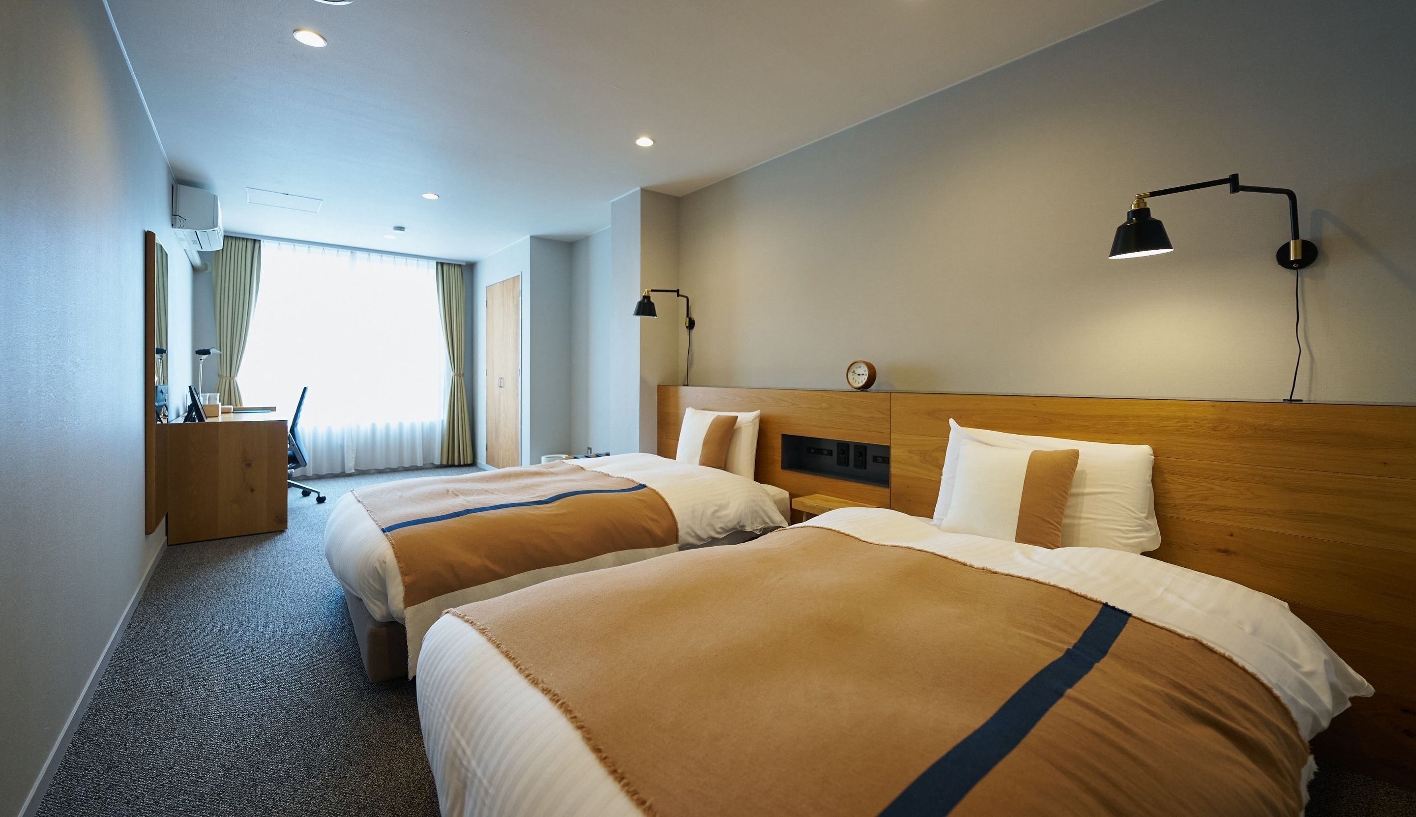 Une chambre d’hôtel avec deux lits, un bureau, une lampe et une fenêtre avec des rideaux.