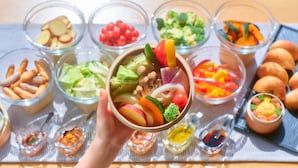 Diversos alimentos em tigelas e pequenas travessas, incluindo frutas, legumes e nozes, dispostos sobre uma mesa.