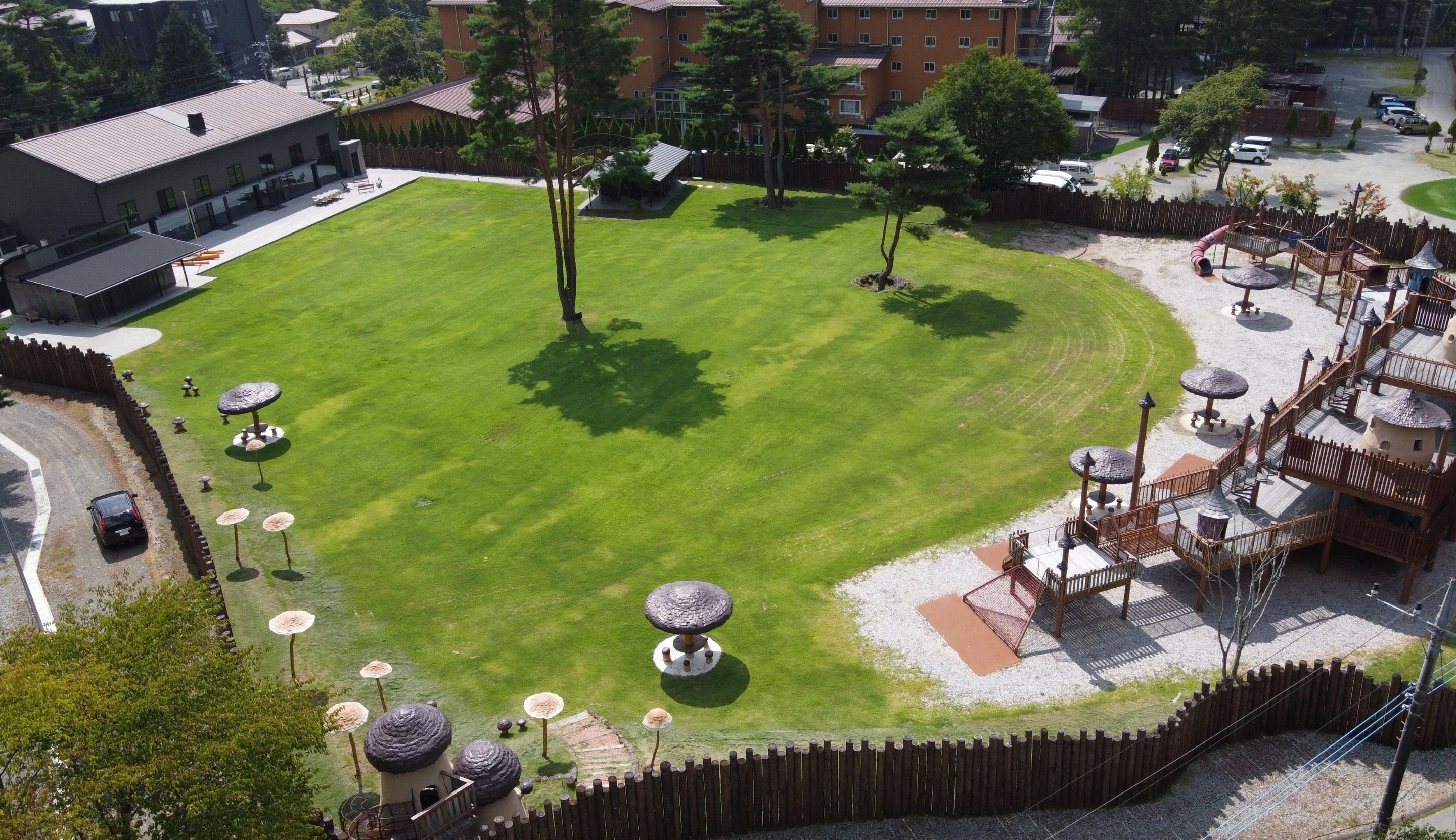Un césped bien cuidado con un parque infantil, un área cercada y un edificio al fondo.