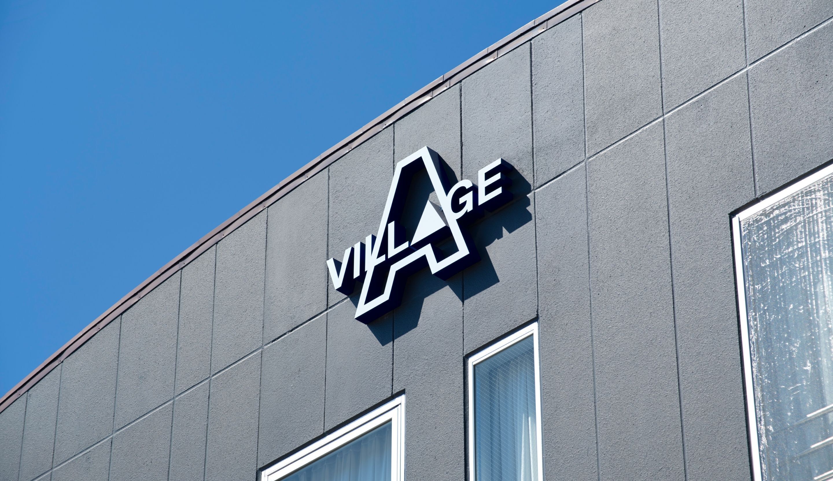 A building with a sign that reads 'VILLAGE' on a grey facade.