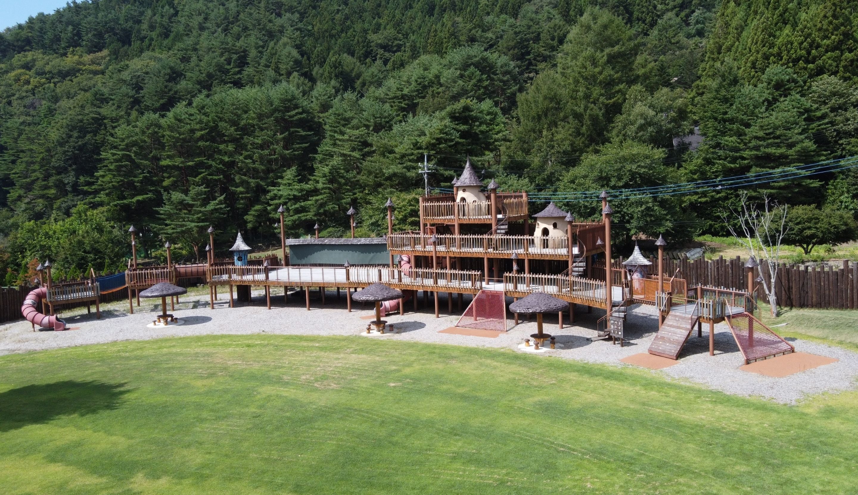 Un parque infantil con un estructura de madera para escalar, toboganes y una zona delimitada por una valla.