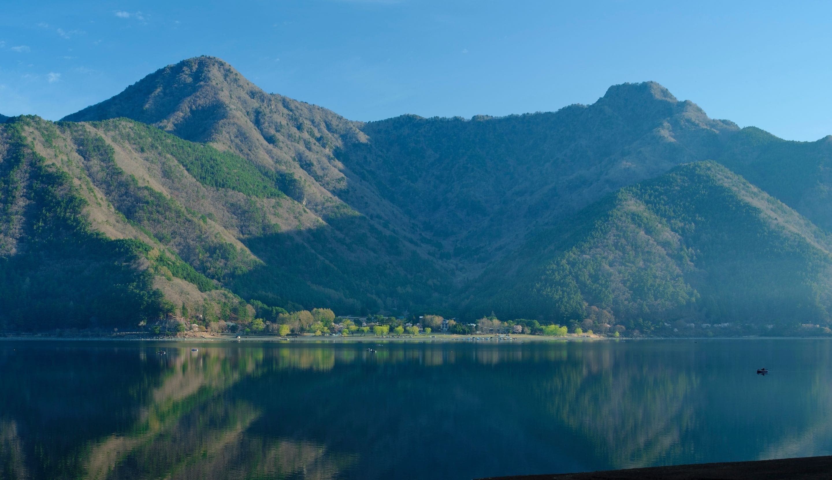 Paisagem montanhosa com um lago em primeiro plano e uma aldeia aos pés das colinas.