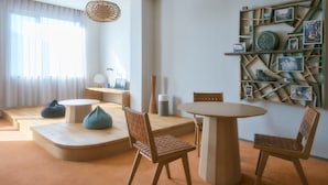 Uma sala de estar moderna com uma mesa redonda, duas cadeiras, um sofá e uma estante na parede com quadros.