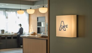 A modern interior with a kitchen area, a person in the background, and a wall-mounted sign with the letters 'CAFÉ'. - A VILLAGE (Fujikawaguchiko)