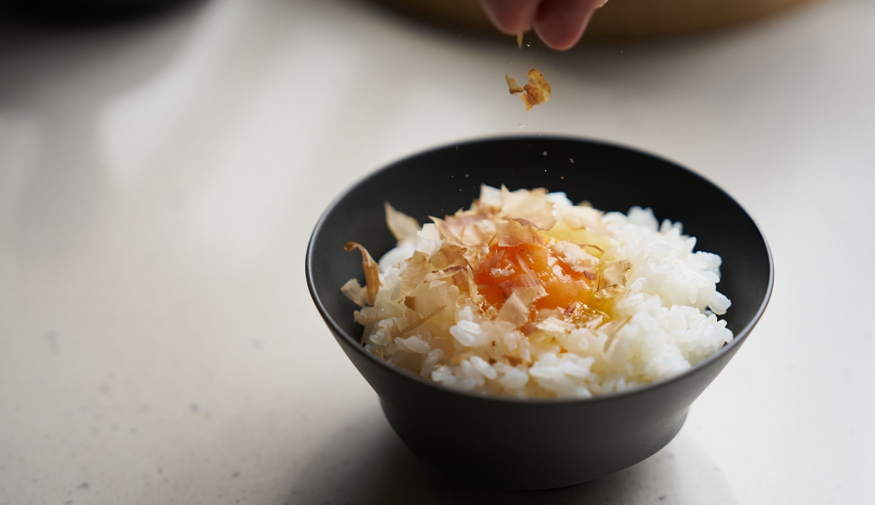 Un tazón de arroz blanco con ingredientes desmenuzados, posiblemente verduras o carne, sobre una superficie blanca.