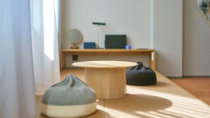 A room with a round wooden table, two bean bags, a desk with a computer and a lamp, and a mirror on the wall. - A VILLAGE (Fujikawaguchiko)