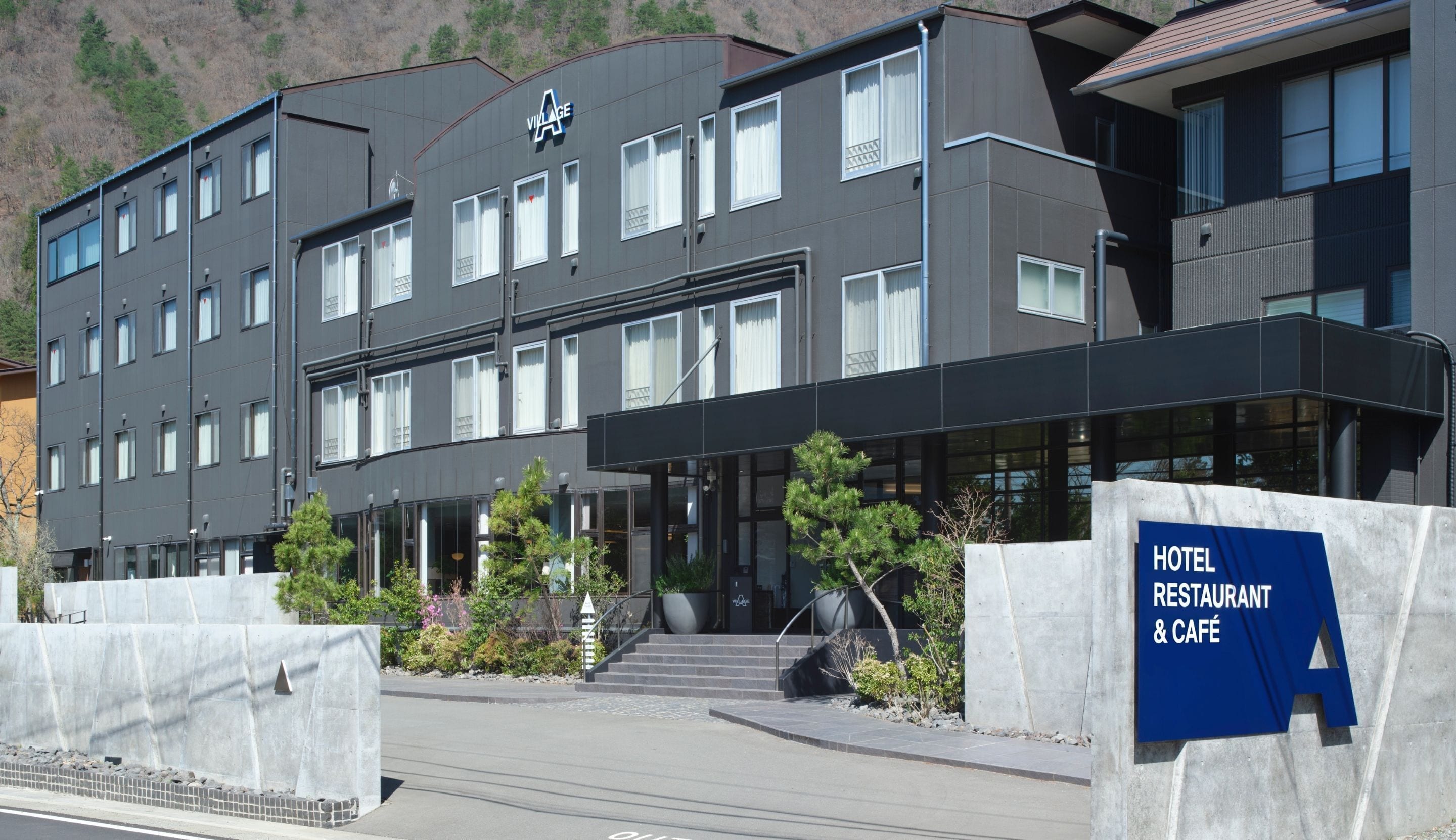 A modern hotel building with a flat roof, multiple windows, and a sign indicating a restaurant and café.