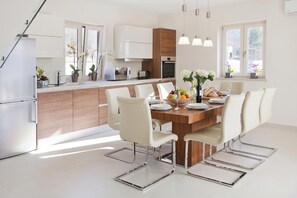 A modern kitchen with white cabinets, a wooden island, and a dining area with a large table and chairs. - Pool Villa Royal Blue /w Panoramic Sea View, Labin, Croatia (Labin)