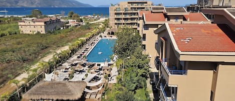 A resort with a swimming pool, lounge areas, and a view of the sea and mountains.