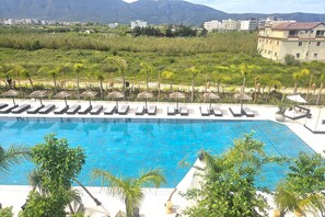 A swimming pool with lounge chairs and palm trees, surrounded by greenery and buildings in the background. - Pool Side Apartment, Vlore, Albania (Vlore)