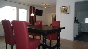 A dining area with a table and chairs, a television on the wall, and a kitchen area. - Oberm Dorp in Winterberg-Hildfeld by Interhome (Winterberg)