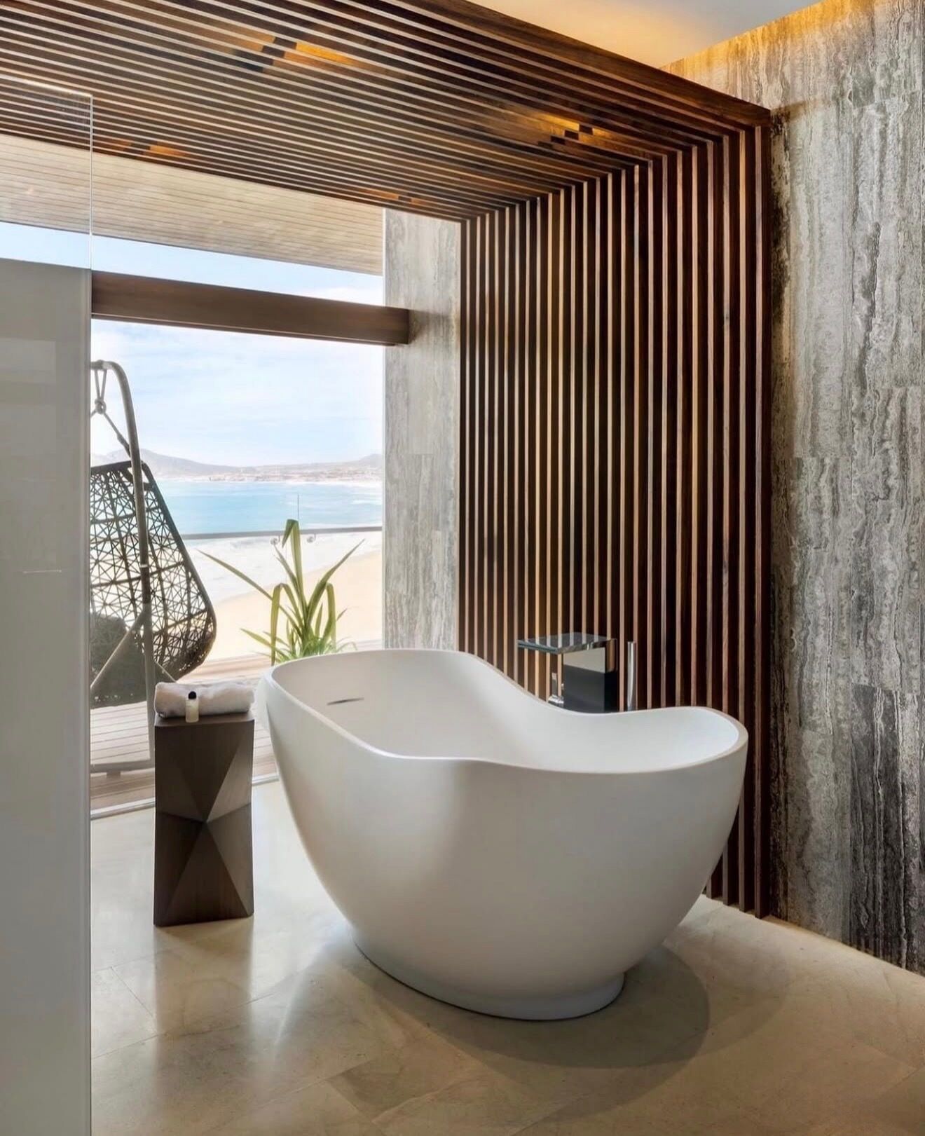 Ein modernes Badezimmer mit einer freistehenden Badewanne, einem geometrischen Beistelltisch und Meerblick.