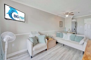 A living room with a white sofa, a standing fan, and a flat-screen TV displaying 'BIG FISH Rentals'. - 1BR, A Relaxing  Place to Stay  Near the the Beach (Myrtle Beach)