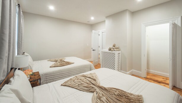 A bedroom with two beds, a nightstand, a lamp, a wooden dresser, and a door.