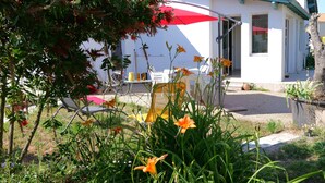 Een wit gebouw met een rode parasol, een terras met stoelen en een tuin vol bloemen.