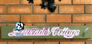 Eine Ziegelwand mit einem Schild, das 'Lavender Cottage' zeigt, und einem Logo mit einer Katze und dem Text 'Haustiere erlaubt'.