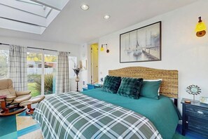 Un dormitorio con una cama grande, una silla, un cuadro y vistas al exterior.