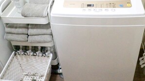 Une machine à laver blanche, dotée d’un panneau de commande, un panier rempli de serviettes pliées et une bouteille de savon liquide.