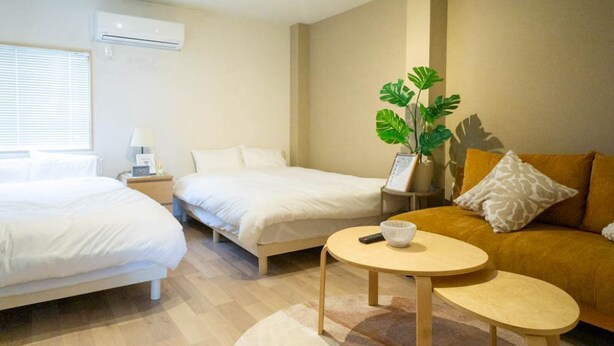 Une chambre d’hôtel avec deux lits, un canapé, une petite table, un climatiseur et une plante.