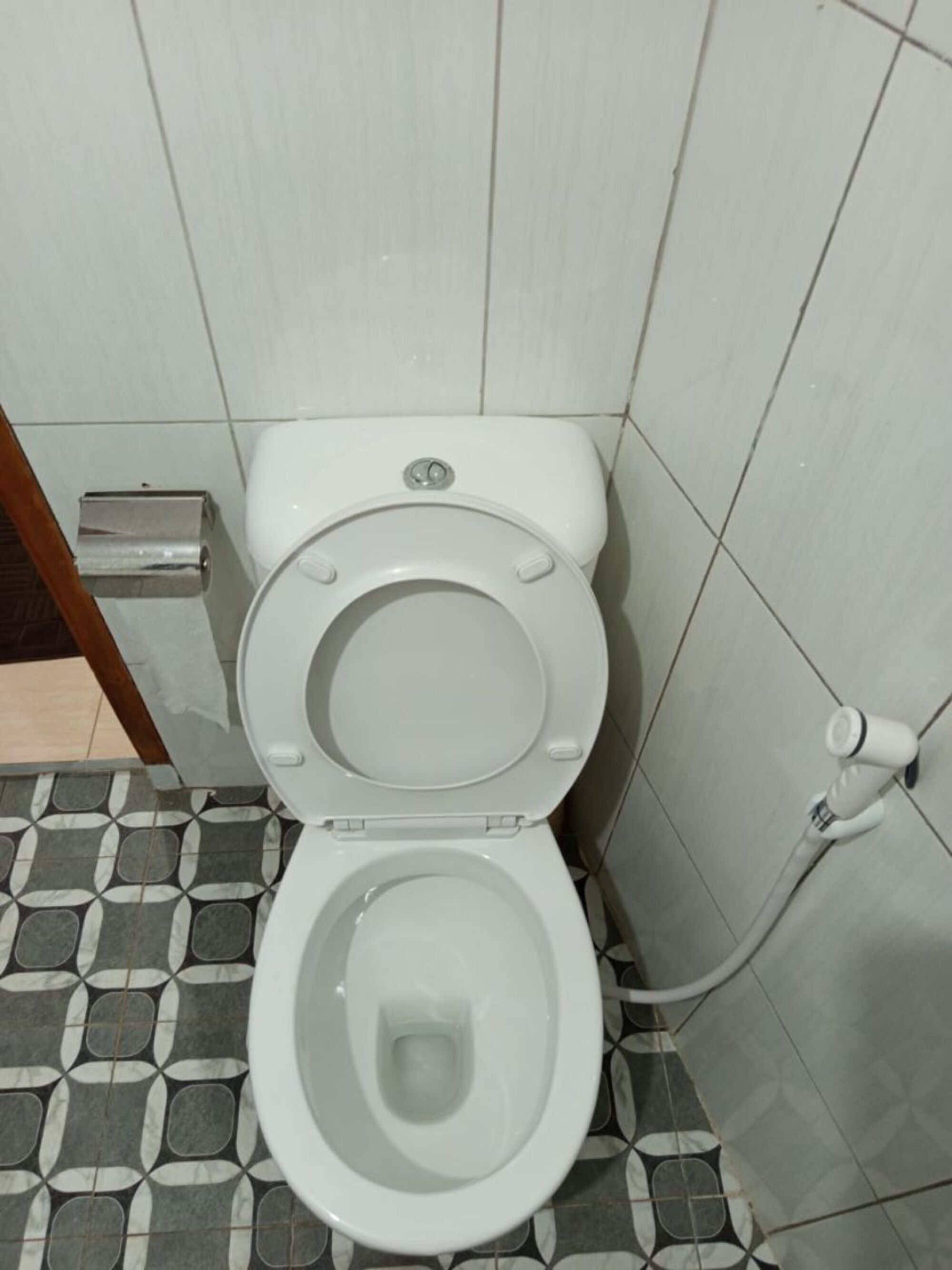 Des toilettes avec un abattant et un couvercle blancs, une poignée de chasse d’eau et un bouton de chasse d’eau fixé au mur.