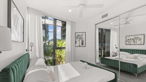 Une chambre d’hôtel moderne avec un grand lit, un balcon agrémenté de plantes, un grand miroir et des œuvres d’art aux murs.