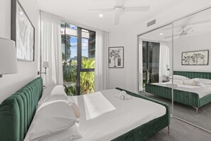 Ein modernes Hotelzimmer mit einem großen Bett, einem Balkon mit Pflanzen, einem großen Spiegel und Kunstwerken an den Wänden.