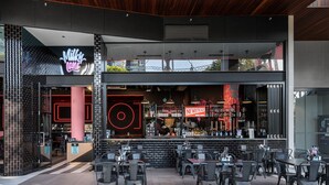 Un espace extérieur moderne aménagé avec des tables et des chaises, un bar agrémenté d’un néon, et une entrée bien visible menant à un restaurant.