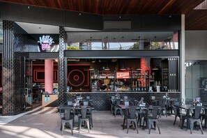 Ein moderner Außenbereich mit Tischen, Stühlen und einer Bar mit Neonbeleuchtung, sowie ein einsehbarer Eingang zu einem Restaurant.
