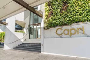 Ein moderner Gebäudeeingang mit Treppe, Wandbegrünung und einem Schild mit der Aufschrift 'Capri'.