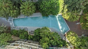 Vue aérienne d’un hôtel doté d’une piscine entourée d’une végétation luxuriante, de nombreux balcons et d’une architecture moderne.