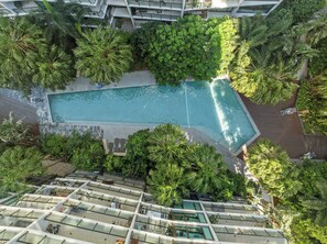 Eine Vogelperspektive eines Hotels mit Schwimmbad, umgeben von üppiger Vegetation, mehreren Balkonen und modernem Architekturstil.