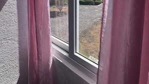 A window with pink curtains, a clear sky, and a view of a mountain.