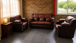 A living room with a brick wall, leather sofas, a wooden side table, and a window with a view.
