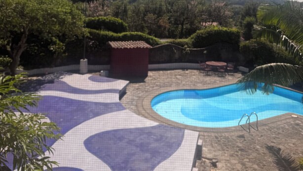 A pool area with a mountain in the background, surrounded by greenery and a clear sky.