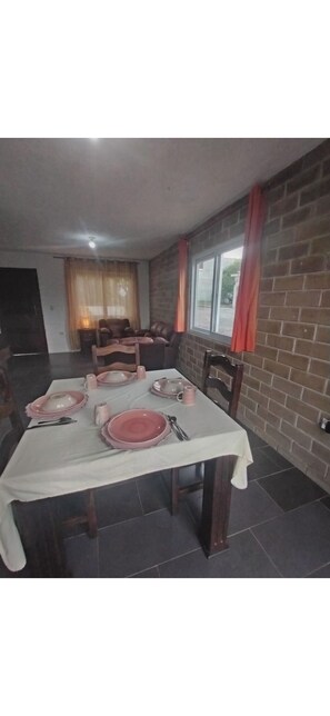 A dining area with a table set for four, chairs, a brick wall, and a window with curtains.