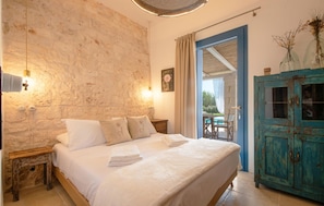 Ein Schlafzimmer mit Steinsandsteinwand, einem Bett mit weißen Leinen, einem hölzernen Nachttisch, einer blauen Tür und einem rustikalen Schrank.