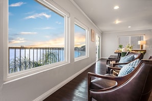 A spacious balcony with a view of the water and sunset, wooden flooring, and leather chairs. - Bay Breeze - Sand and Sun (San Diego)