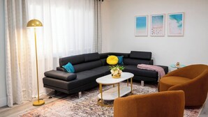Ein modernes Wohnzimmer mit einem schwarzen Ecksofa, einem runden Couchtisch, einer Stehlampe und einem kleinen runden Tisch mit einer Lampe.