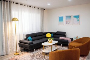 A modern living room with a black sectional sofa, a round coffee table, a floor lamp, and a small round table with a lamp. - Rock Waterfall Pool | FIFA Base | Bold Design (Wilton Manors)