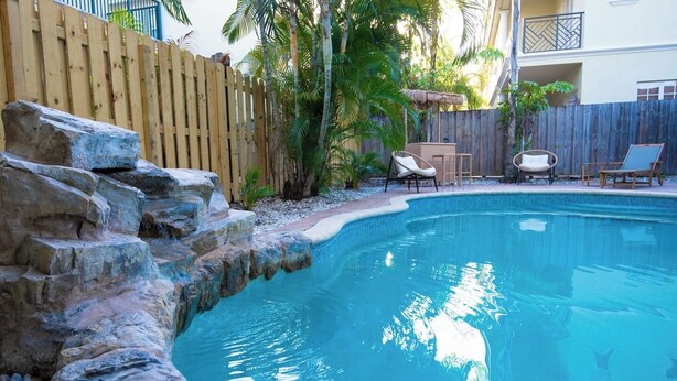 Ein Pool mit Holzzaun, Palmen und Gartenmöbeln.