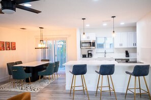 A modern kitchen with white cabinets, a central island, bar stools, and a dining table with chairs. - Rock Waterfall Pool | FIFA Base | Bold Design (Wilton Manors)