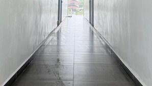 A long, narrow hallway with tiled floors and plain walls, leading to a bright area with a view of the outside.