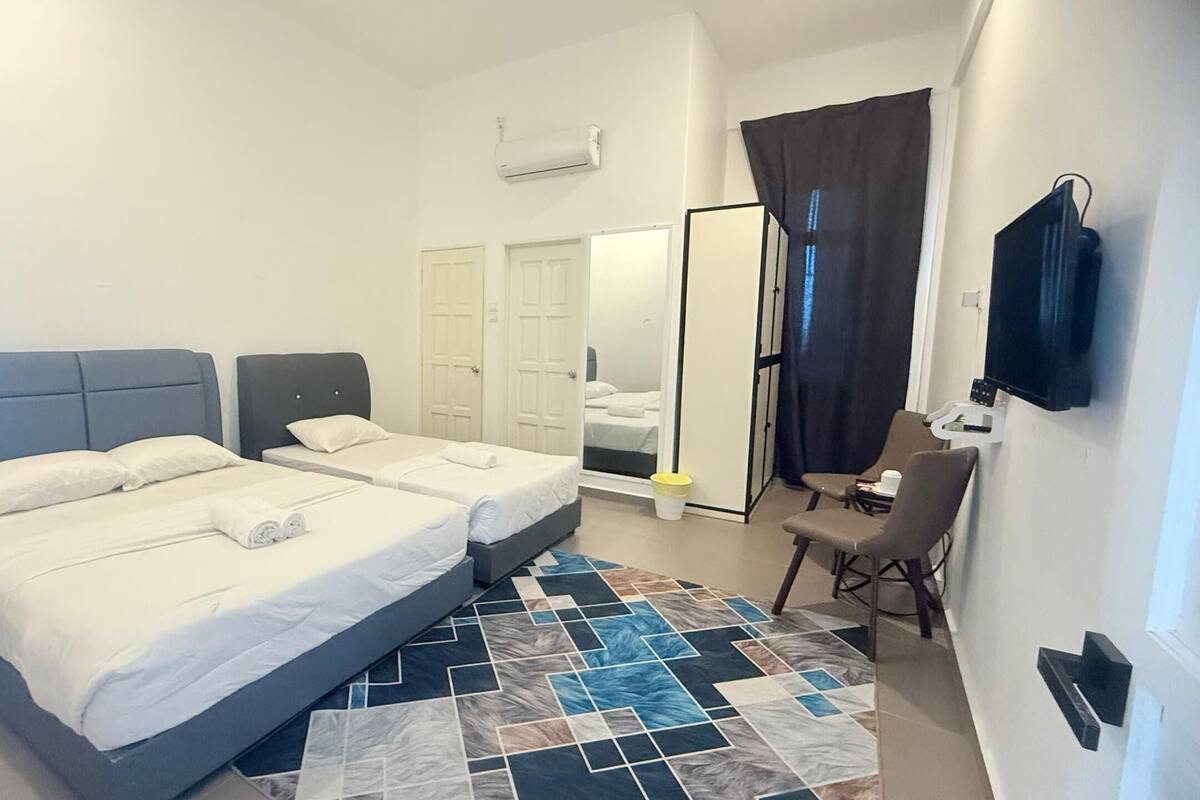 A hotel room with two beds, a TV, a chair, and a bathroom visible through an open door.