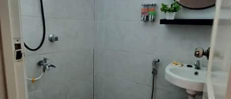 Um banheiro pequeno com azulejos, chuveiro, pia e espelho.