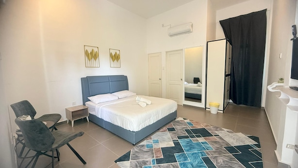 A bedroom with a bed, a chair, a nightstand, an air conditioning unit, and a door leading to another room.