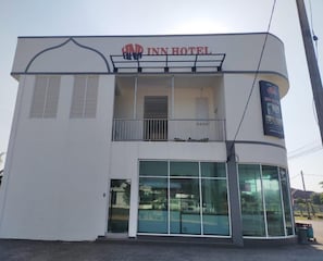 Un bĂątiment Ă deux Ă©tages, dotĂ© dâun balcon Ă lâĂ©tage supĂ©rieur, de grandes fenĂȘtres en verre au rez-de-chaussĂ©e et dâune enseigne indiquant « INN HOTEL » au-dessus de lâentrĂ©e.