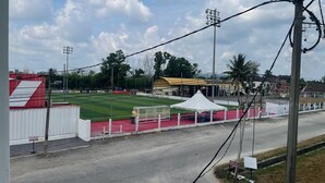 A sports field with a white tent, a red and white building, and a road with a sign.