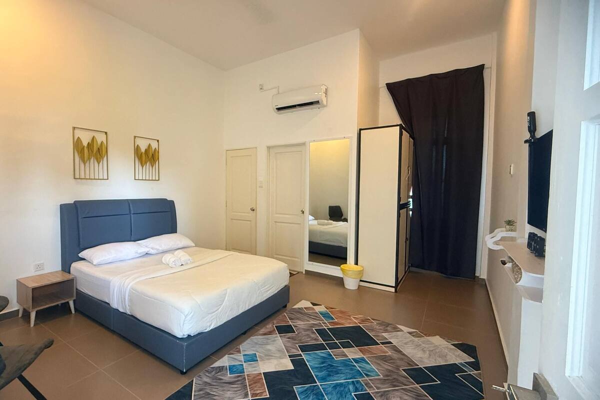 A bedroom with a bed, a chair, a nightstand, a rug, and a door leading to another room.